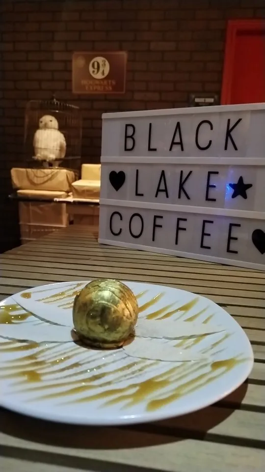 Postre dorado en forma de esfera con alas frente al letrero luminoso del café